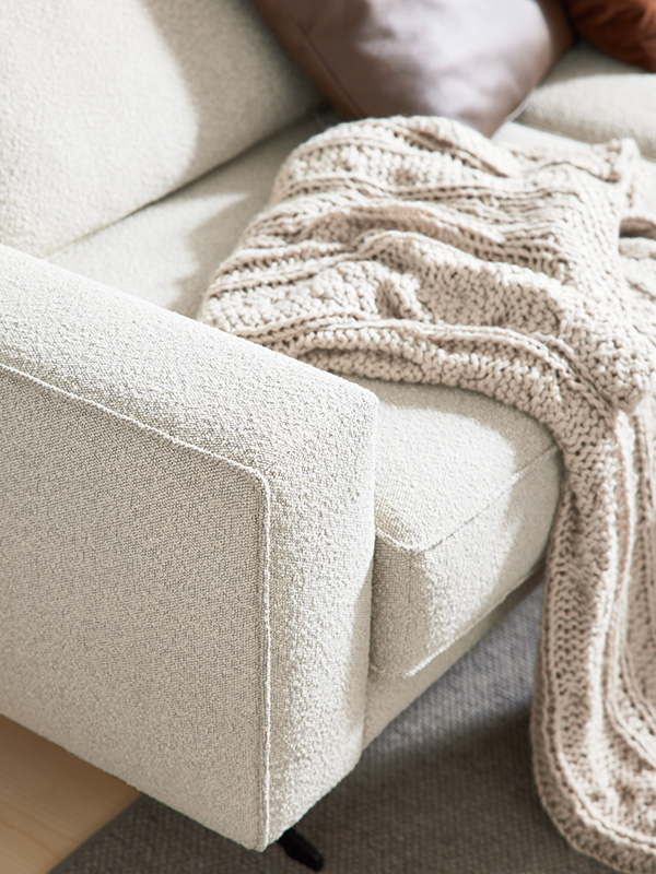 Detailaufnahme von einer Armlehne eines hellen Sofas mit heller Kuscheldecke
