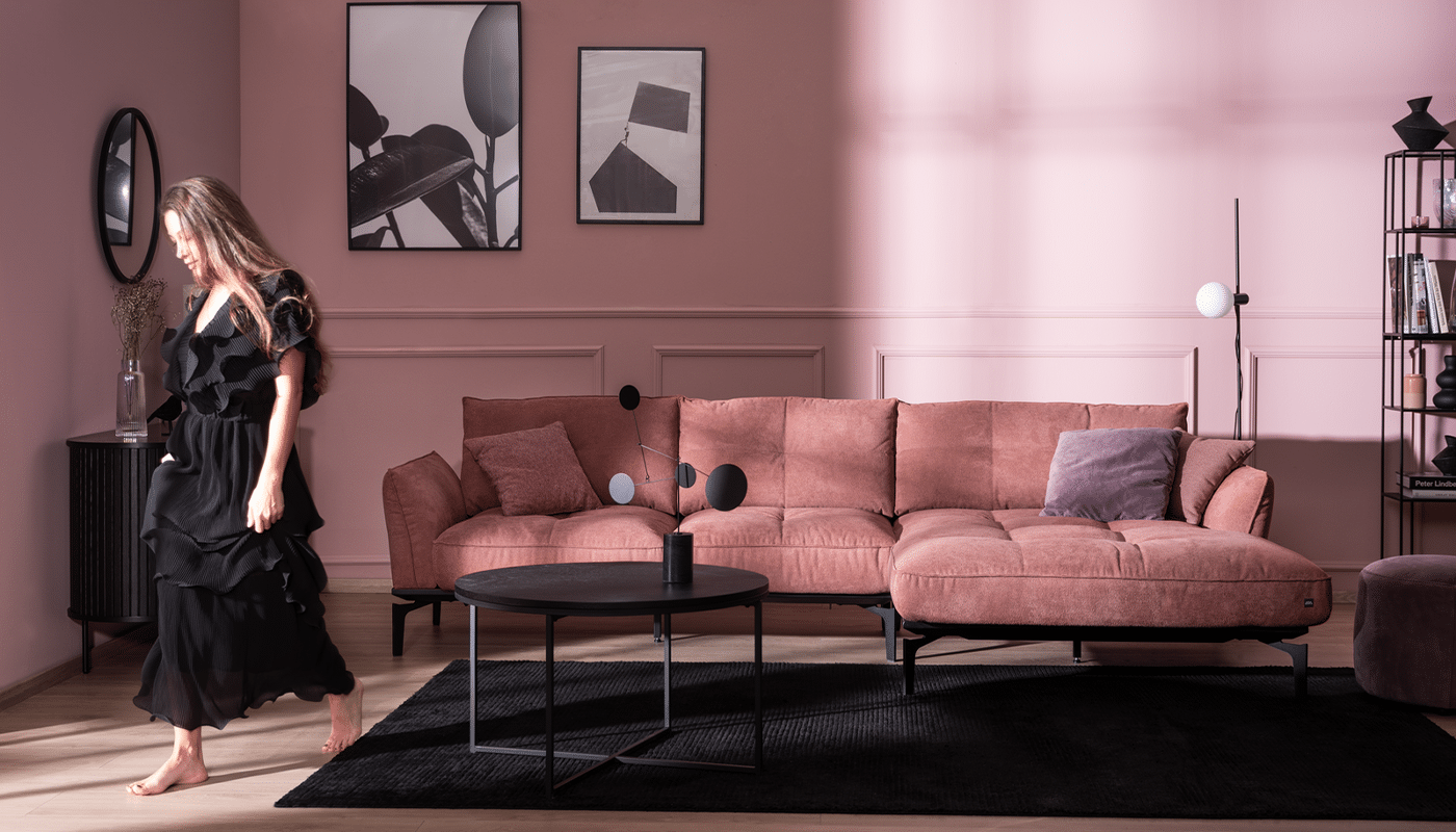 4xl-CALTHA (3) Die Sonne scheint in das rosa Wohnzimmer mit schwarzen Highlights, Frau trägt ein schwarzes Kleid