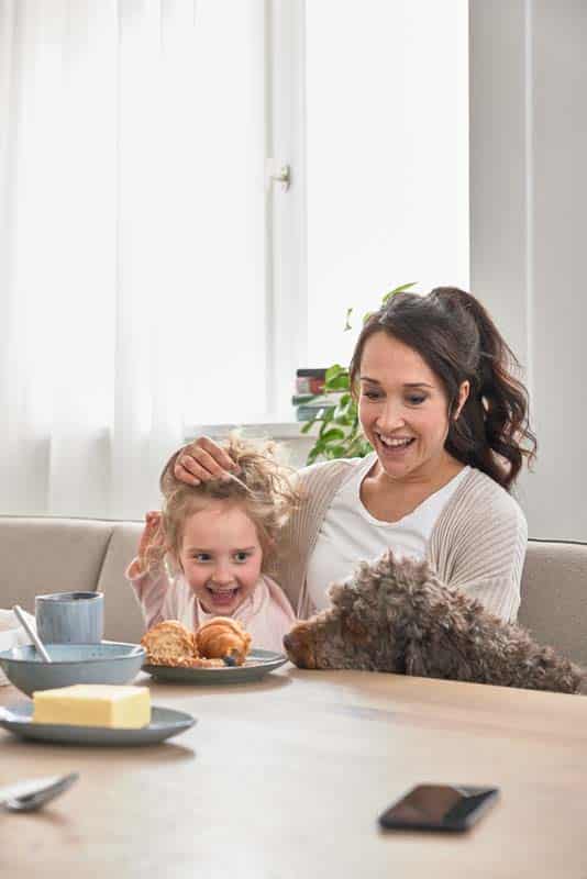 Mutter mit Kind und Familienhund beim Frühstückstisch