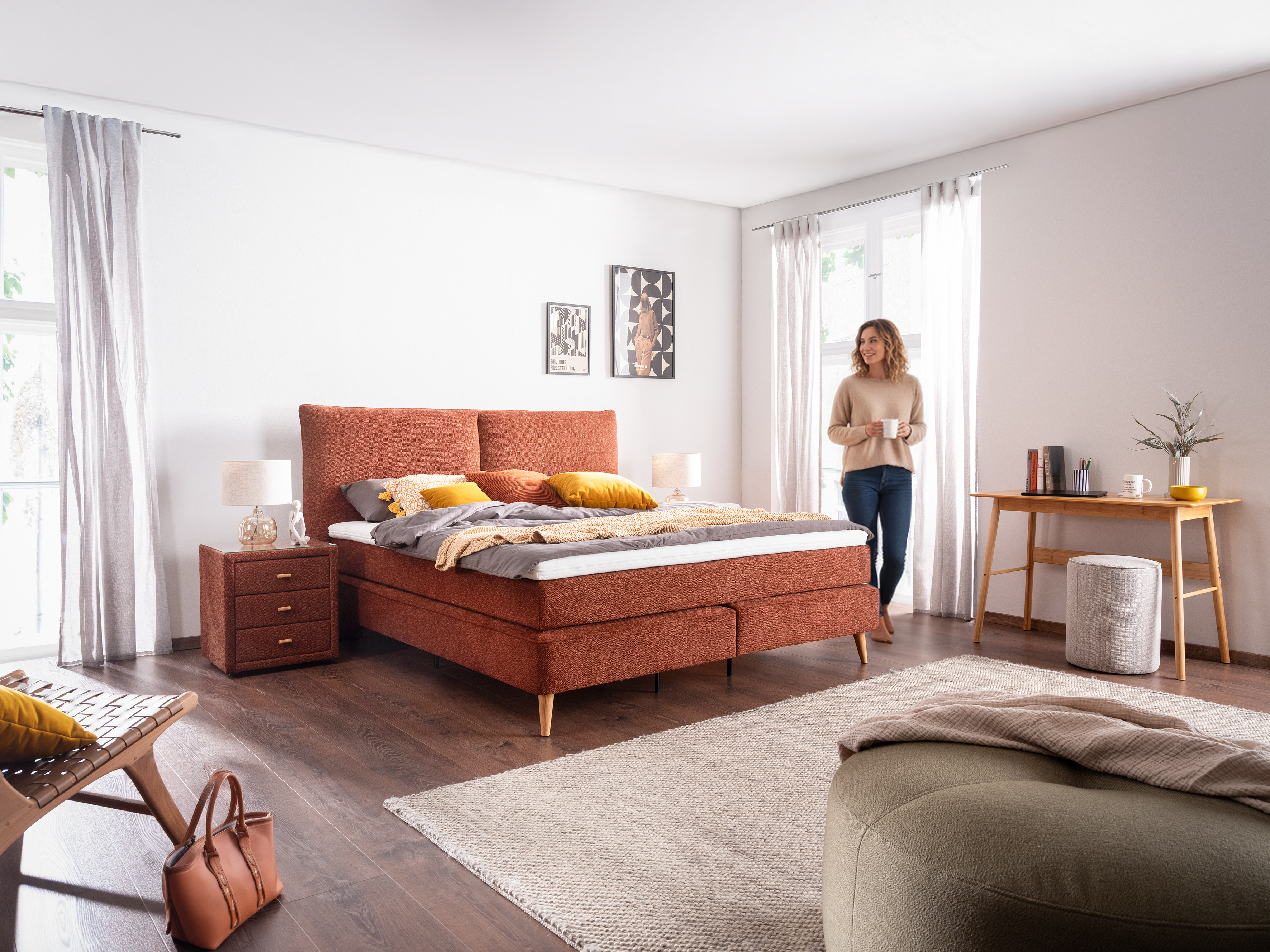 Frau steht mit Tasse neben Boxspringbett NERONI